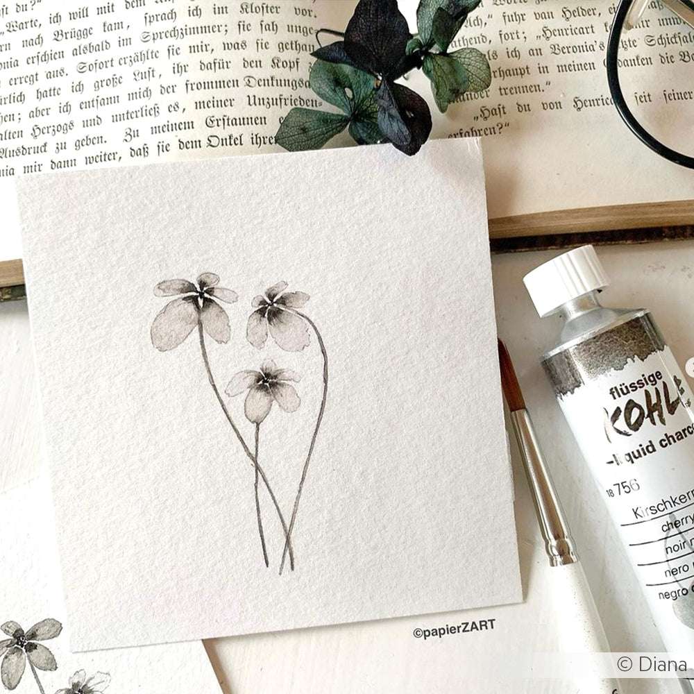 Eine zarte Bleistiftzeichnung von drei Blumen auf strukturiertem Papier, umgeben von Schmincke Aquarellfarben, Kunstzubehör und einem offenen Buch.