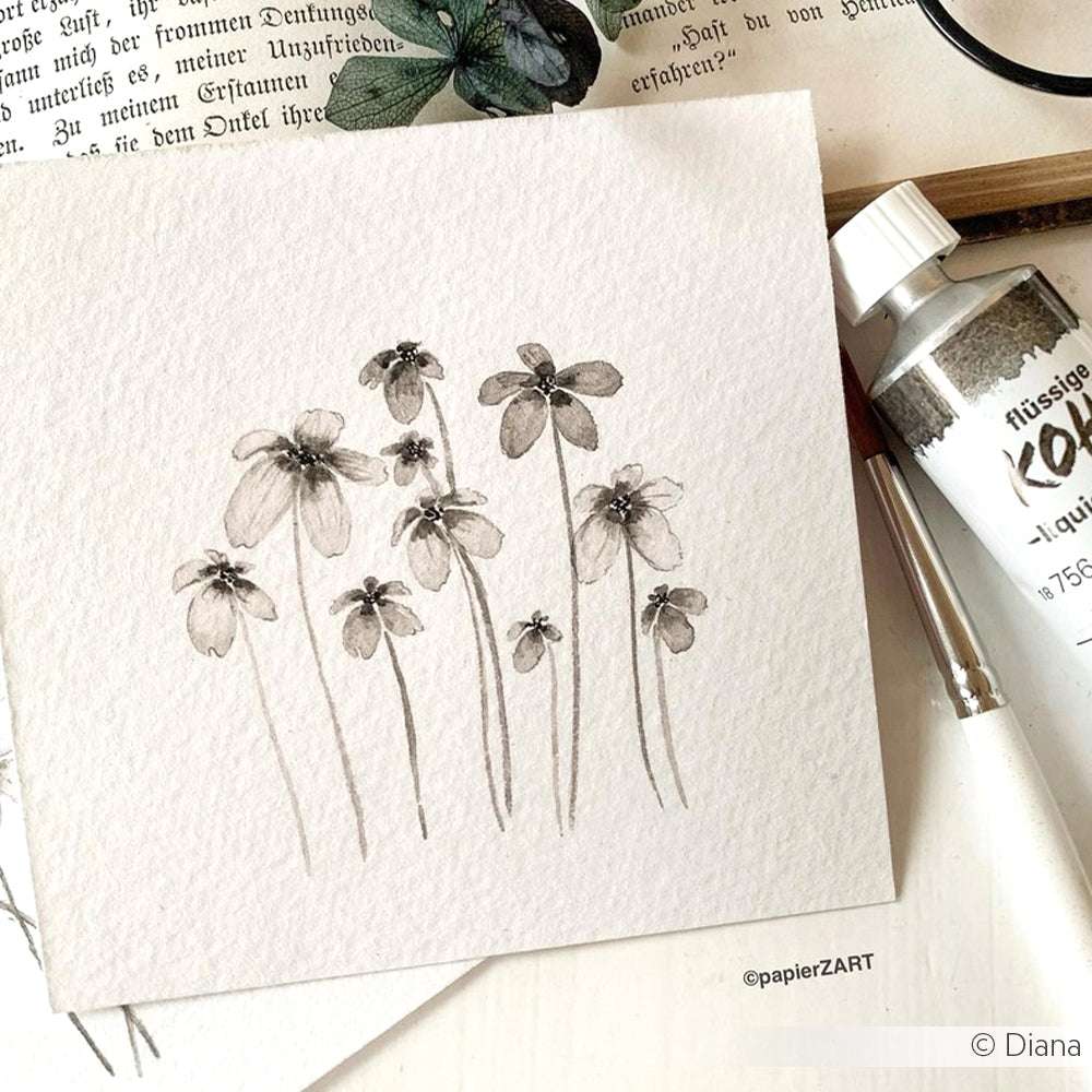 Ein Aquarell mit zarten Wildblumen in gedeckten Tönen auf strukturiertem Papier, in dessen Nähe Schmincke Künstler-Wasserfarben und Kunstzubehör wie Gummi arabicum angeordnet sind.