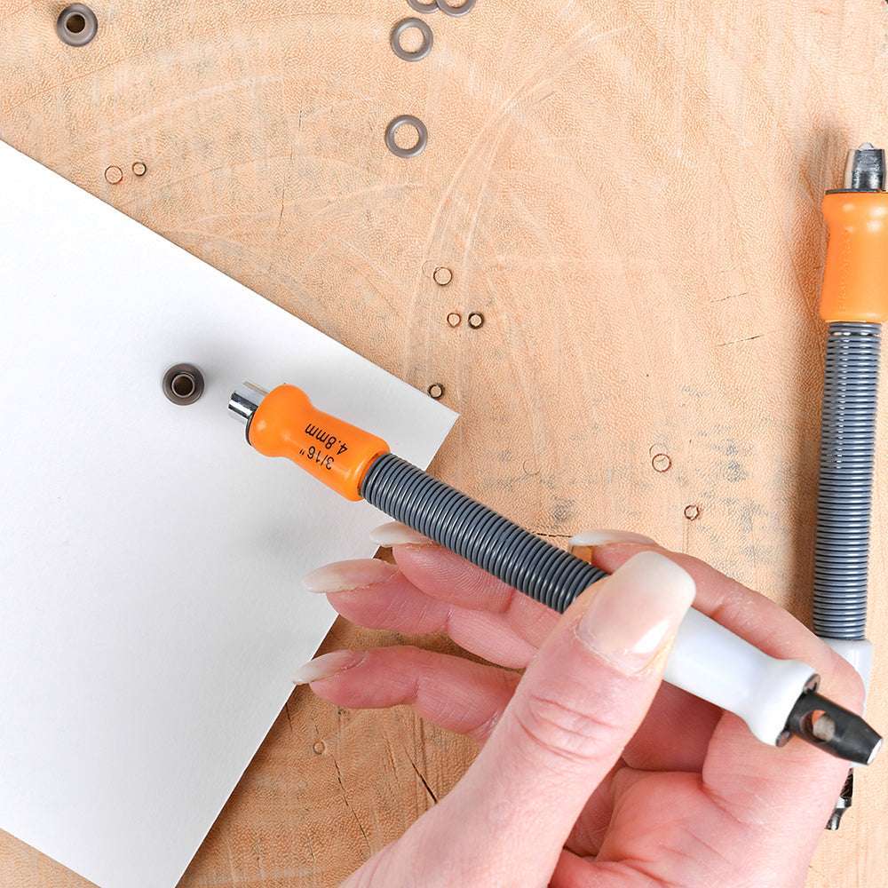 Eine Hand benutzt ein orange-weißes Fiskars-Werkzeug auf weißem Papier, das auf einer Holzunterlage liegt.