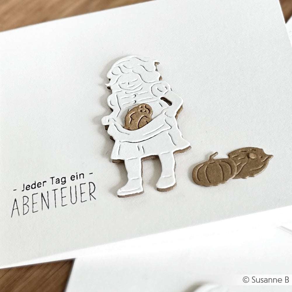 Weiße Karte von Alexandra Renke mit einem ausgeschnittenen Mädchen, das einen Kürbis in der Hand hält, mit zwei Kürbissen daneben und dem deutschen Text "Jeder Tag ein Abenteuer" - perfekt, um Ihre Lieblingsdesignpapiere zu präsentieren oder mit Motivstempeln zu kombinieren.