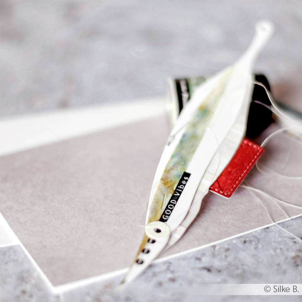 Eine handgefertigte Feder mit dem Text "Good Vibes" ruht auf einem Umschlag und Papier, umgeben von Alexandra Renke Garnspulen und hübschen Designpapieren, perfekt zum Basteln mit Motivstanzen.