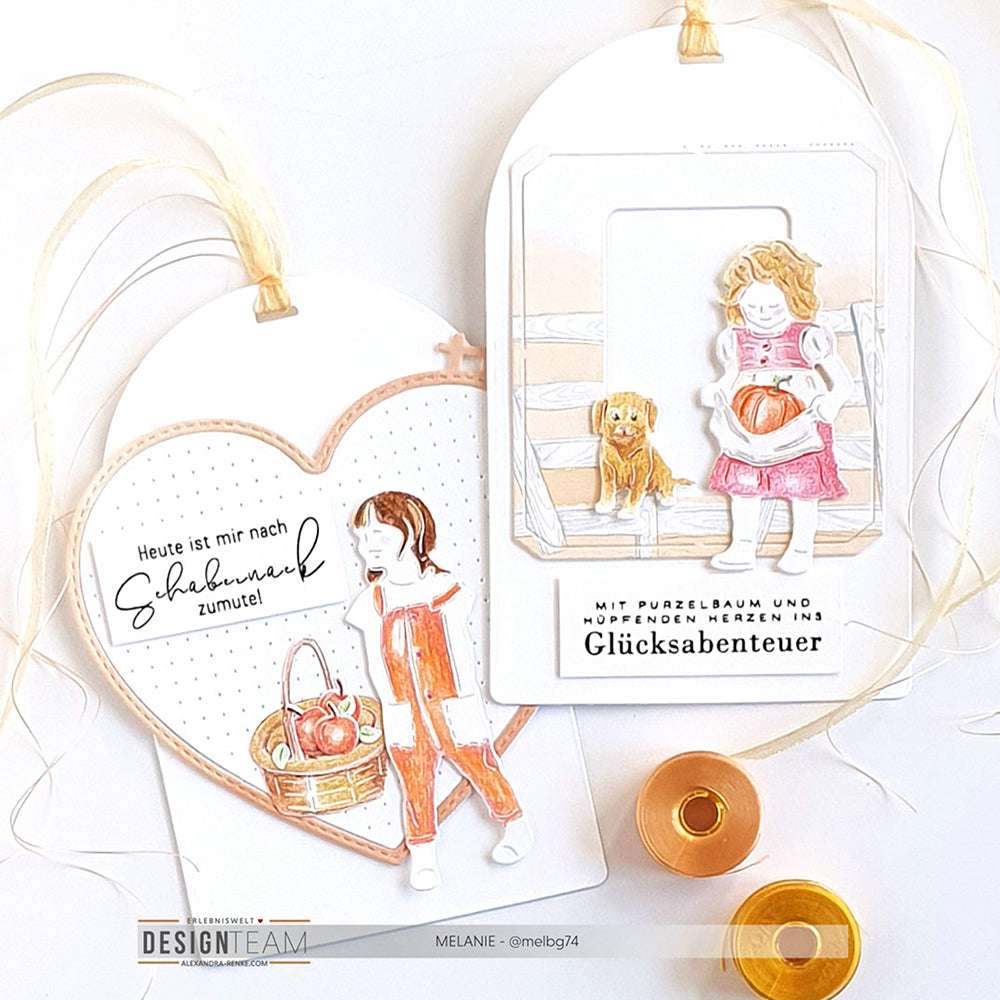 Zwei herzförmige Anhänger von Alexandra Renke mit illustrierten Mädchen, einem Hund, Körben und deutschem Text mit Bandakzenten - ideal für Ihre Designpapiere-Projekte oder als Ergänzung zu jeder Motivstanze-Kollektion.
