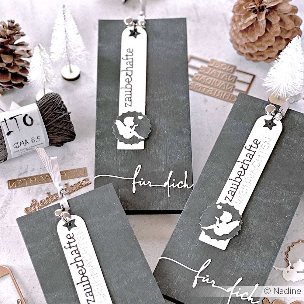 Geschenkschachteln mit weihnachtlichen Lesezeichen, Tannenzapfen, Garn und Mini-Bäumchen, arrangiert mit charmanten Details, die mit Alexandra Renke Stanzen und Motivstanze wie Etikett Lang Anhängern geschnitten wurden.