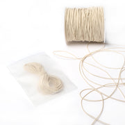 Eine Spule beigefarbenes Elastikband von Alexandra Renke mit einem kleinen Bündel in einem durchsichtigen Beutel, ideal für Bastelprojekte, dargestellt auf weißem Hintergrund.