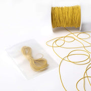 Eine Spule und ein Bündel dünnes gelbes Alexandra Renke Elastikband, mit einem Bündel in einem durchsichtigen Plastikbeutel auf weißem Hintergrund - perfekt für jedes Bastelprojekt.