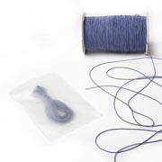 Eine Spule dünnes blaues Elastikband, eine lose Länge und ein kleines Bündel Gummibänder von Alexandra Renke in einem durchsichtigen Plastikbeutel auf weißer Oberfläche.