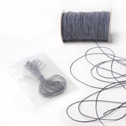 Graue Spule Alexandra Renke Elastikband mit loser Kordel daneben; aufgerollte Gummibänder in einem Klarsichtbeutel - ideal für Ihr nächstes Bastelprojekt.
