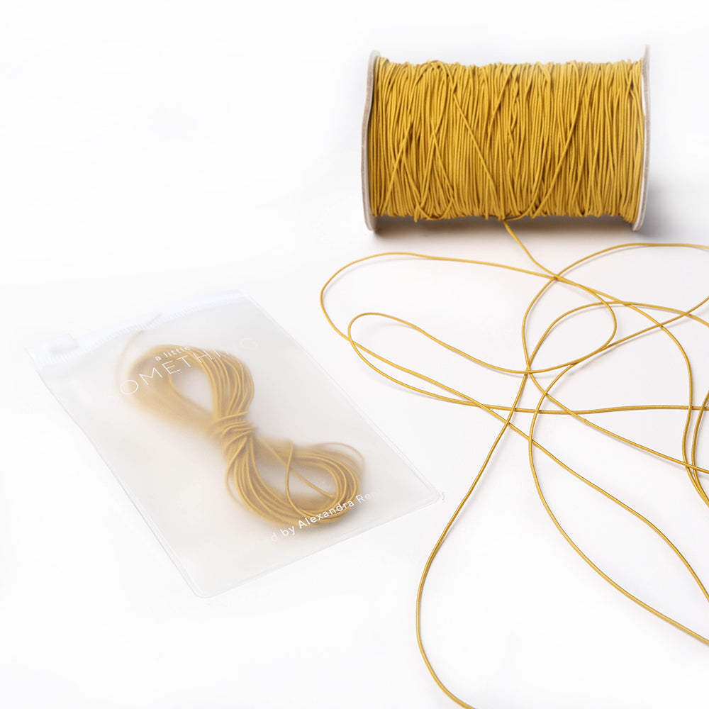 Eine Spule und ein kleines Bündel senfgelbes Elastikband von Alexandra Renke liegen auf einer weißen Fläche, perfekt für Ihr nächstes Bastelprojekt.