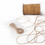 Eine Spule und ein Bündel hellbraunes Elastikband von Alexandra Renke, mit etwas loser Kordel auf einer weißen Fläche - ideal für Ihr nächstes Bastelprojekt.