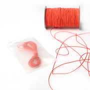 Eine Spule mit dünnen orangefarbenen Alexandra Renke Gummibändern liegt neben einem durchsichtigen Beutel mit einer aufgewickelten Länge der gleichen Schnur - ideal für jedes Bastelprojekt.