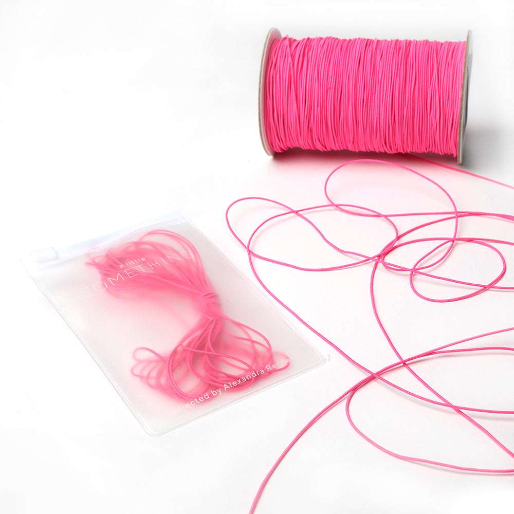 Eine Spule und ein Bündel hellrosa Elastikband von Alexandra Renke sind auf weißem Hintergrund abgebildet, ideal für Ihr nächstes Bastelprojekt.