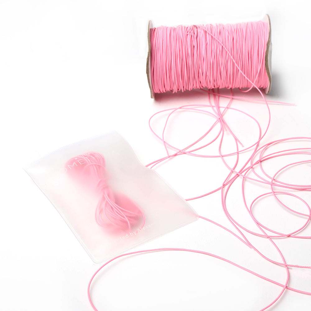 Eine Spule rosa Elastikband von Alexandra Renke mit losen Strängen und einer gebündelten Portion, ordentlich aufbewahrt in einem halbtransparenten Beutel - ideal für Ihr nächstes Bastelprojekt.