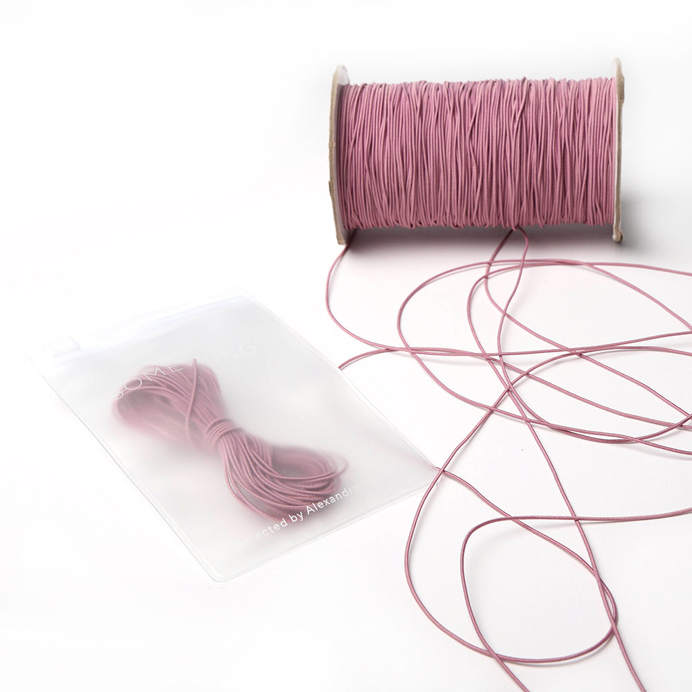 Eine Spule rosa Alexandra Renke Elastikband mit einem kleinen Bündel und loser Schnur in einem durchsichtigen Beutel - ideal für Ihr nächstes Bastelprojekt.