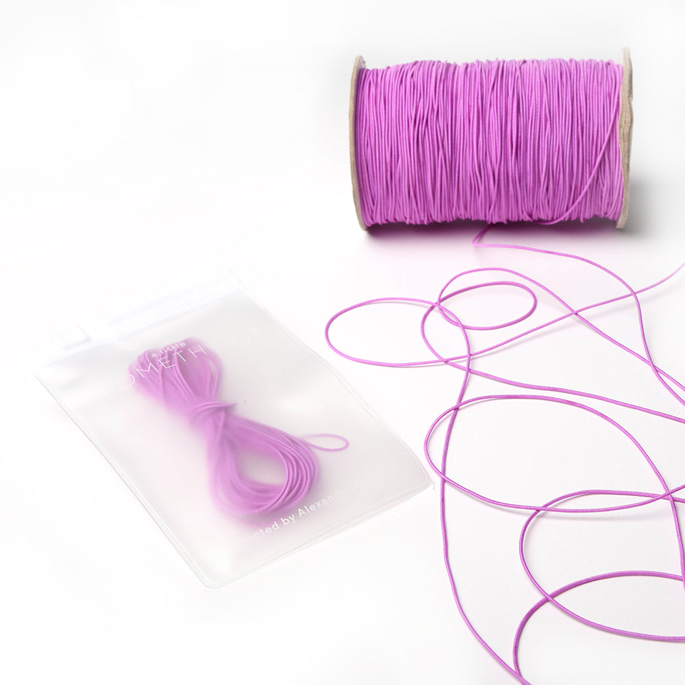 Eine Spule rosa Elastikband von Alexandra Renke mit einem passenden Bündel in einem durchsichtigen Beutel - ideal für Ihr nächstes Bastelprojekt - präsentiert auf einer weißen Fläche.