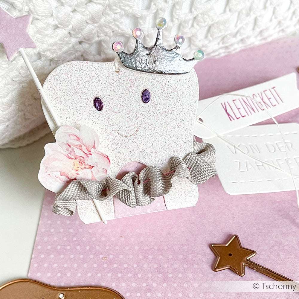 Eine bezaubernde Zahn-Figur mit Krone, Zauberstab und Rüsche erscheint auf einem rosafarbenen Hintergrund mit einem Anhänger und Knöpfen - ideal für Ihr nächstes Alexandra Renke Design oder für die Verwendung mit DieCut Systemen wie der Motivstanze Zahnbox.
