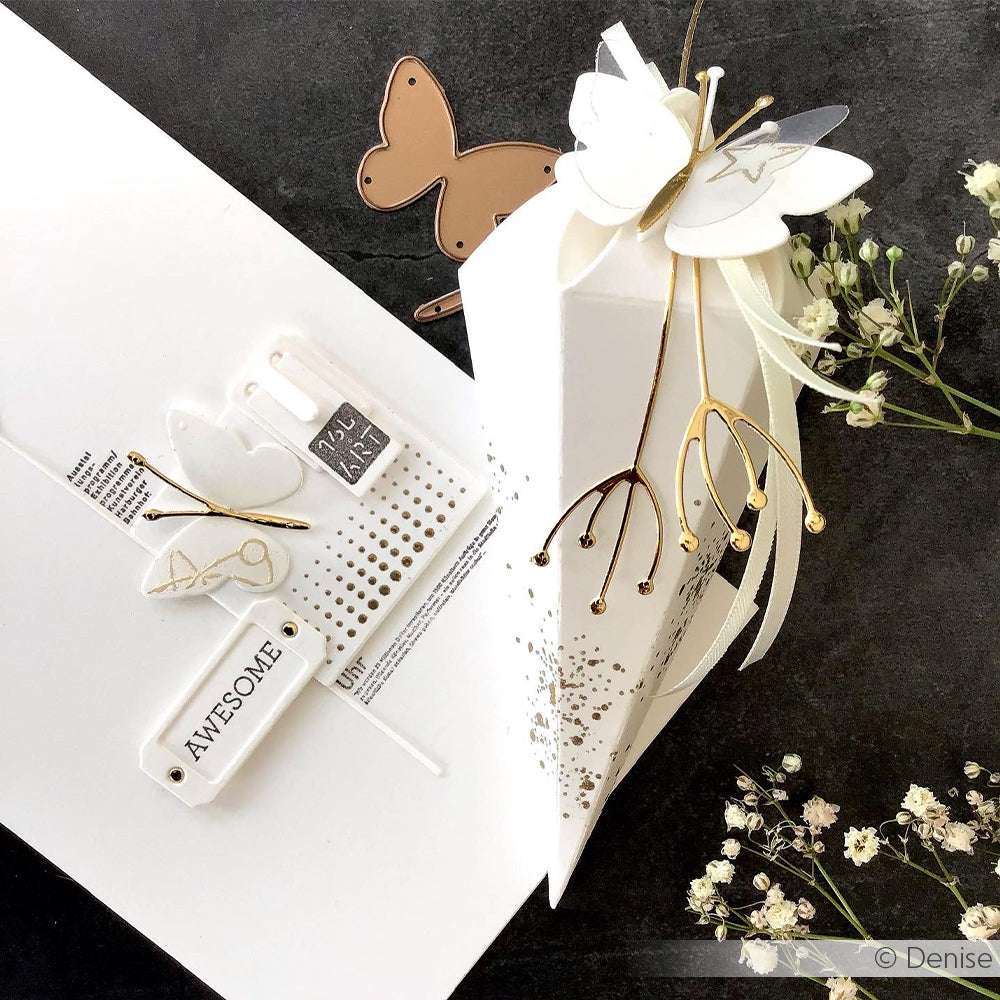 Elegante weiß-goldene Geschenkbox mit Schmetterlingsmotiv von Alexandra Renke aus Designpapier mit Blumendekoration und passender Karte, die auf schwarzem Hintergrund wunderschön zur Geltung kommt.