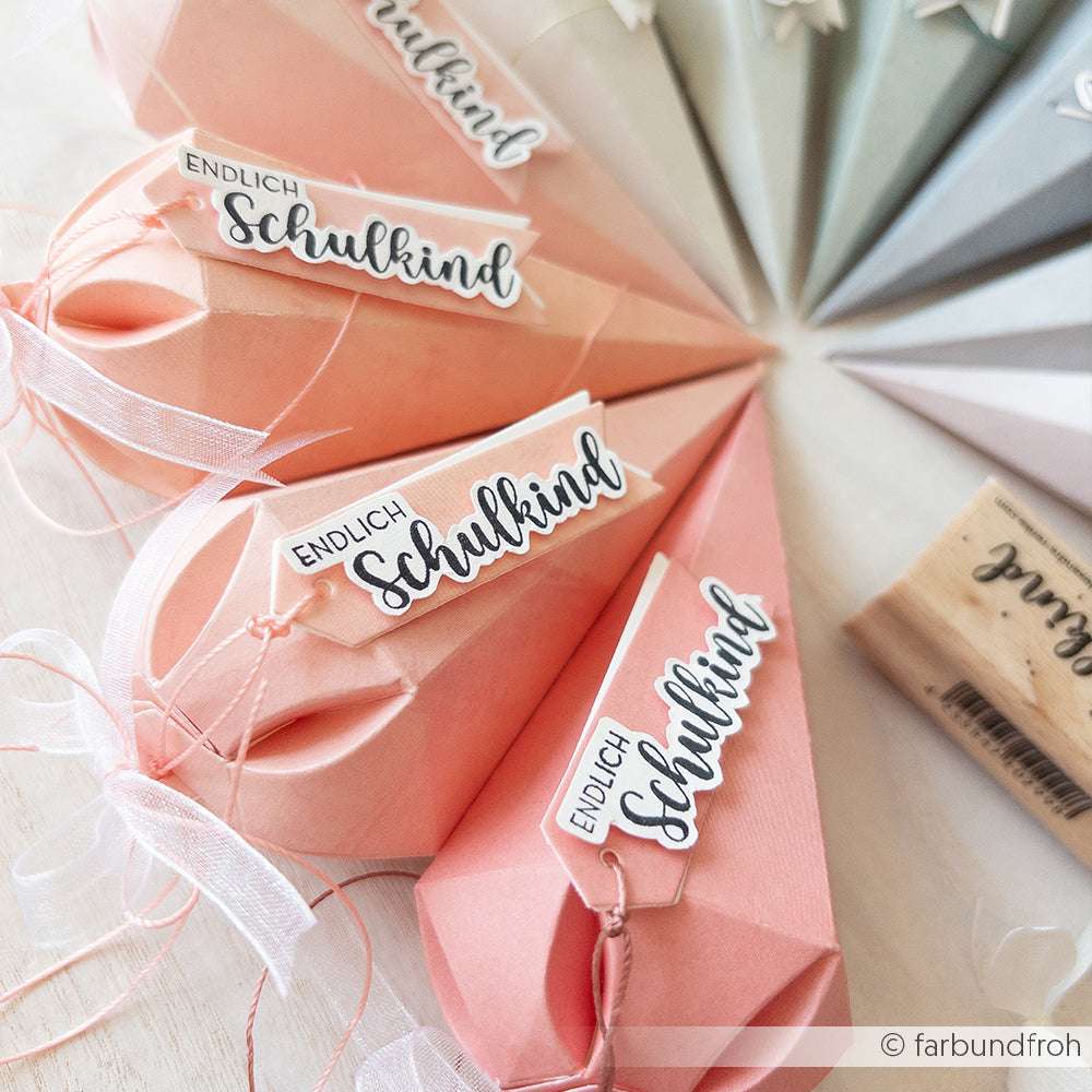 Pastellfarbene Schultüten aus Designpapier von Alexandra Renke, alle mit der Aufschrift Endlich Schulkind" versehen, mit Bändern verziert und ordentlich auf einem Tisch arrangiert.