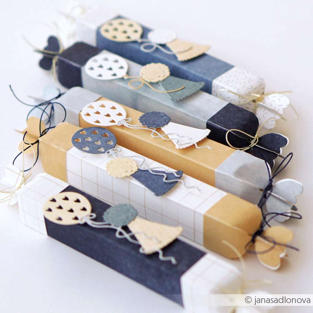 Bunte Geschenke aus Papier, dekoriert mit ausgeschnittenen Figuren, die Luftballons halten, in einer Reihe angeordnet - perfekt, um Alexandra Renke DieCut Systeme zu präsentieren oder die Motivstanze Bonbon-Box 3 auf Ihrem Designpapier auszuprobieren.