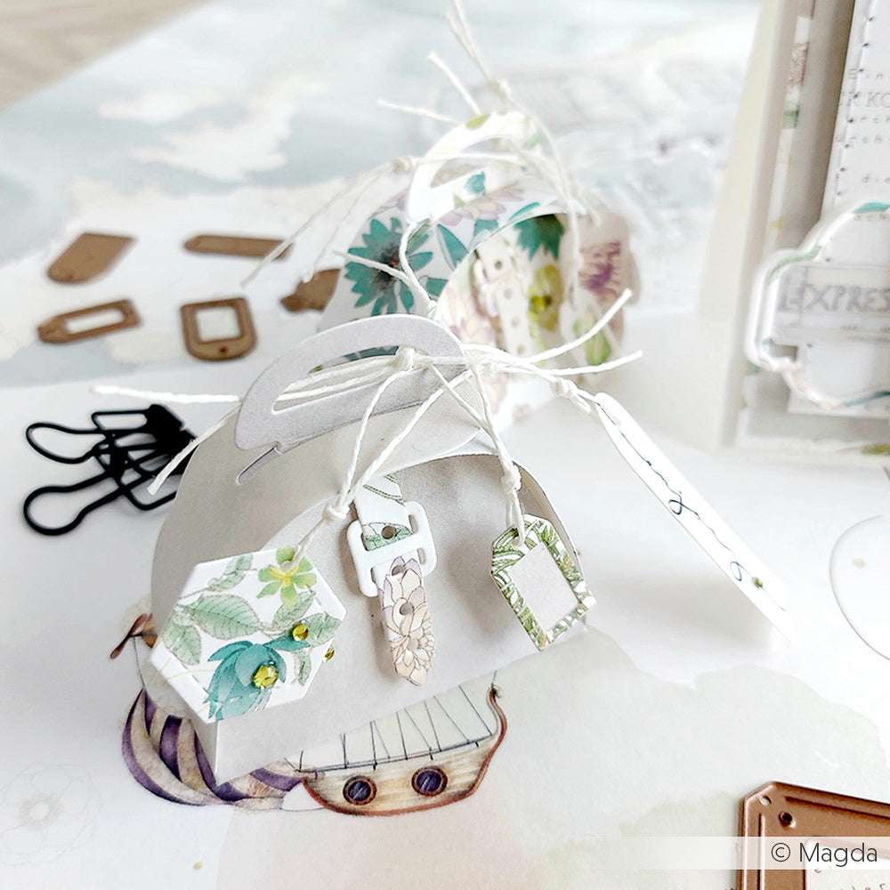 Eine Nahaufnahme von handgefertigten Geschenkanhängern von Alexandra Renke, hergestellt aus floralem Designpapier und befestigt an einem grauen Papierhalter mit weißer Schnur.