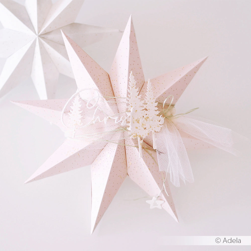 Rosa 3D-Papierstern-Ornament, gefertigt aus Designpapieren und verziert mit weißen Bäumen, Tüll und einem kleinen hängenden Stern auf hellem Hintergrund. Ideal, um die filigranen Designs zu präsentieren, die sich mit Stanzsystemen oder einer Motivstanze „Faltstern“ realisieren lassen.