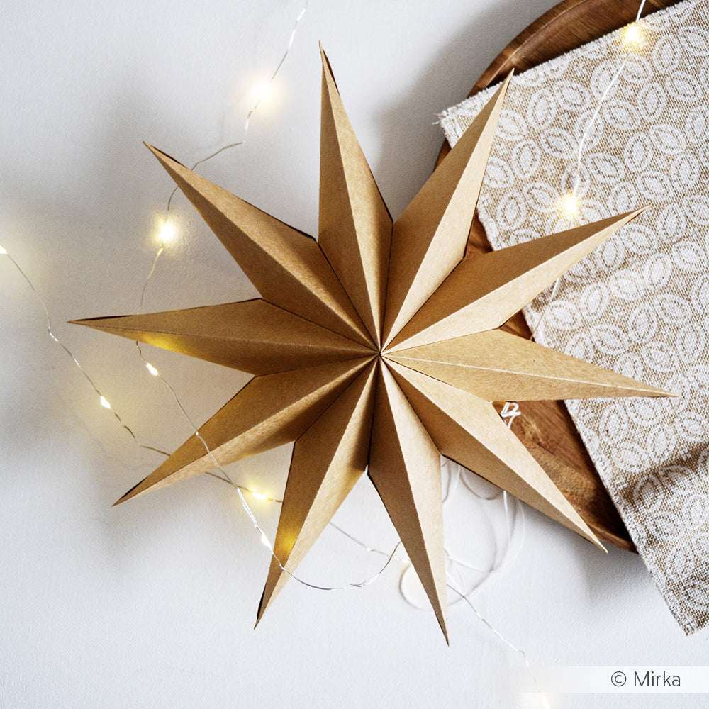 Ein brauner Papierstern schmückt einen Tisch mit einem gemusterten Tuch, einem Holztablett und einer Lichterkette - hergestellt mit Alexandra Renke Designpapieren und dem Motivstanze Faltstern DieCut System für einen charmanten Handmade-Look.