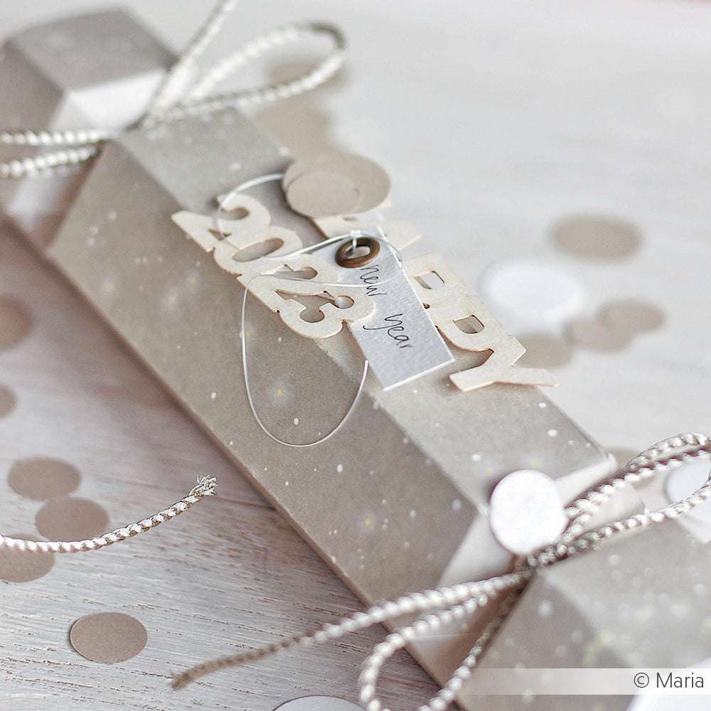 Ein festlicher Cracker, hergestellt mit der Alexandra Renke Motivstanze Knallbonbon, ist mit "2023", Schleife und Konfetti auf hellem Holz verziert - perfekt für kreative Projekte mit Stanzsystemen.