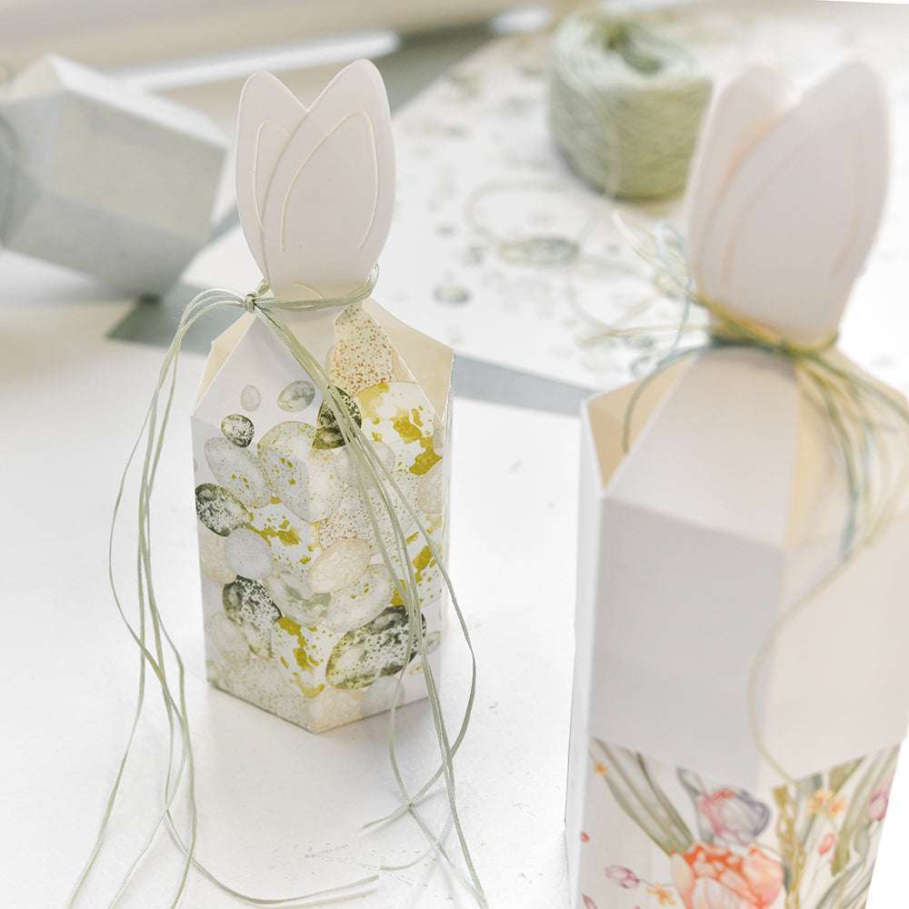 Dekorative florale Geschenkschachteln mit tulpenförmigem Deckel, gefertigt aus leuchtenden Alexandra Renke Designpapieren und mit grüner Schnur verschnürt, ausgestellt auf einer weißen Fläche.