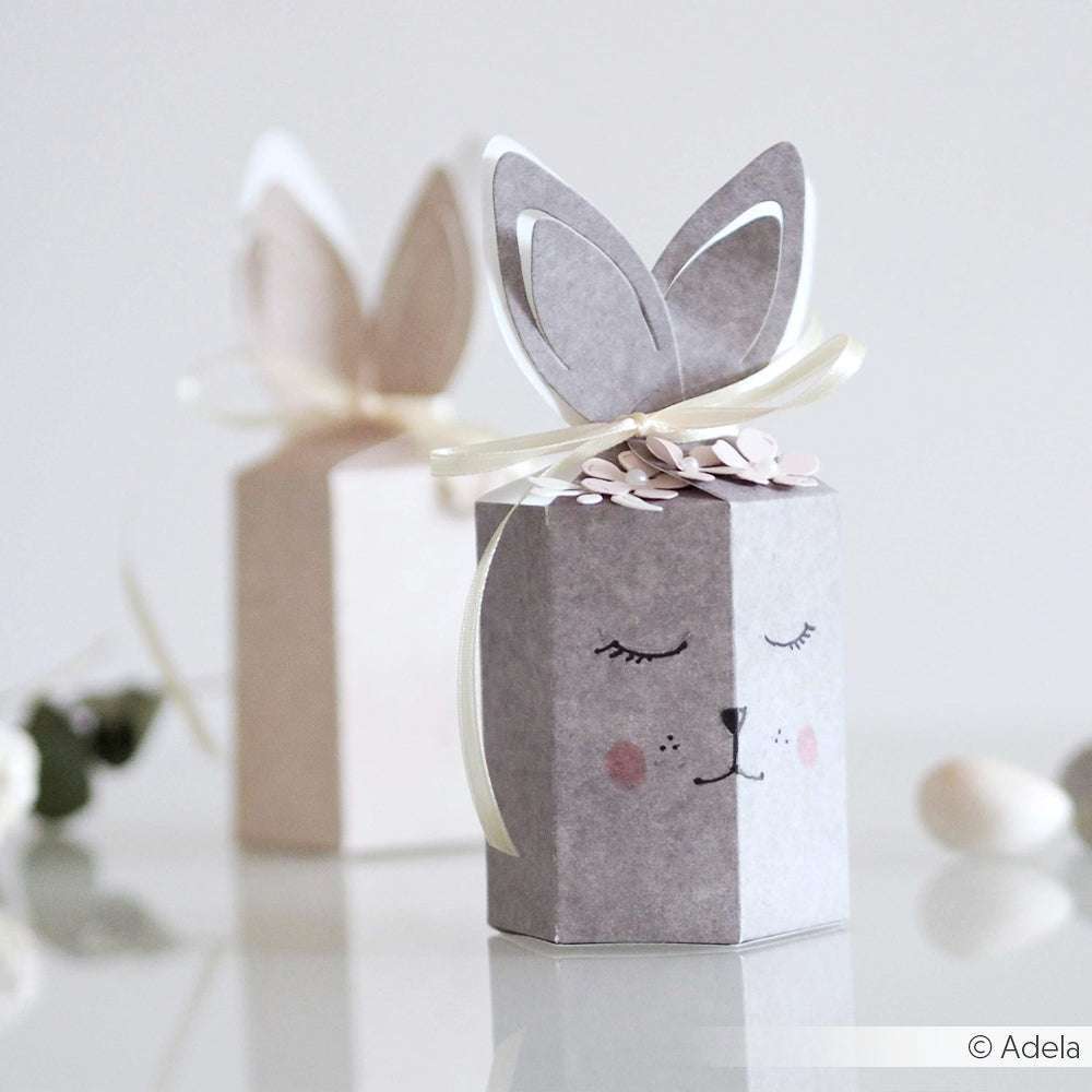 Zwei sechseckige Geschenkschachteln von Alexandra Renke sind mit Designpapier, Schleifenband, gezeichneten Gesichtern und niedlichen Papierohren aus dem Motivstanze Schachtel Hasenohren DieCut System als Häschen gestaltet.