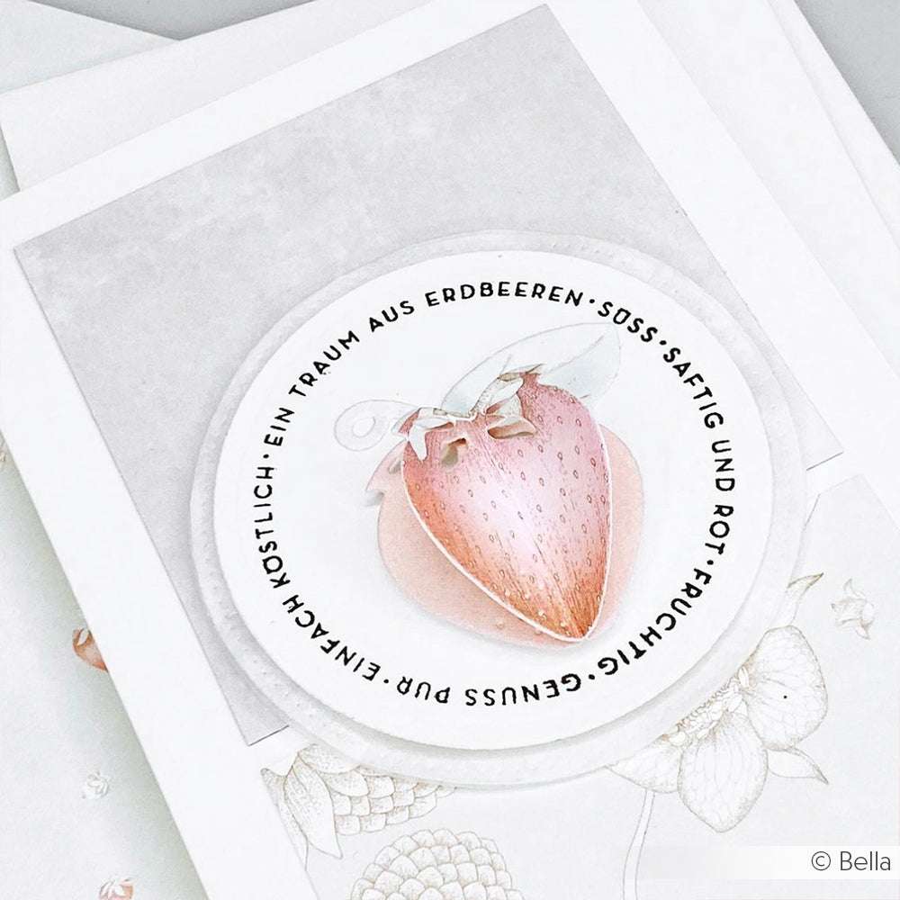 Eine Karte von Alexandra Renke mit einer rosafarbenen Erdbeer-Illustration aus der Motivstanze Erdbeere und einem deutschen Text, der sie umgibt, vor einem weiß-grauen Hintergrund.