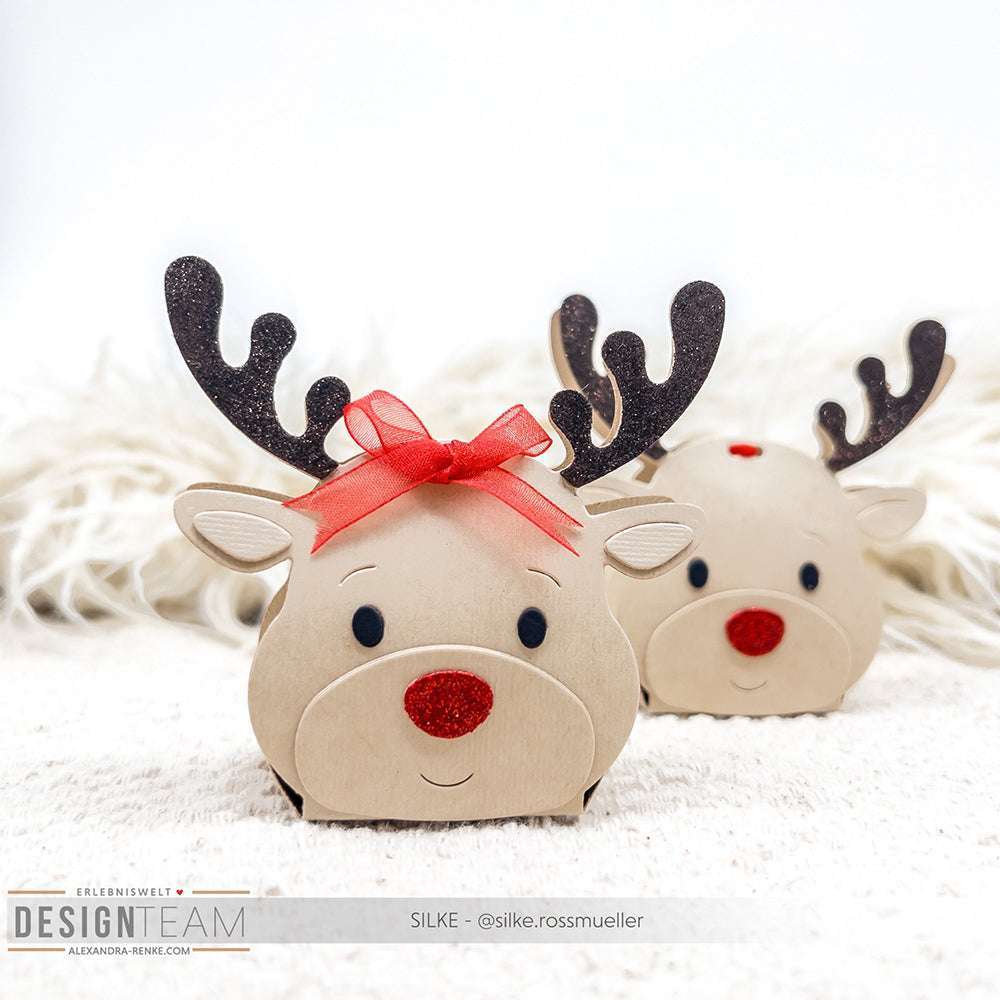 Zwei bezaubernde Rentier-Geschenkboxen, hergestellt mit der Motivstanze Rentier-Box von Alexandra Renke und festlichen Designpapieren, zeigen rote Nasen, schwarze Geweihe und rote Schleifen auf einer weißen Fläche.