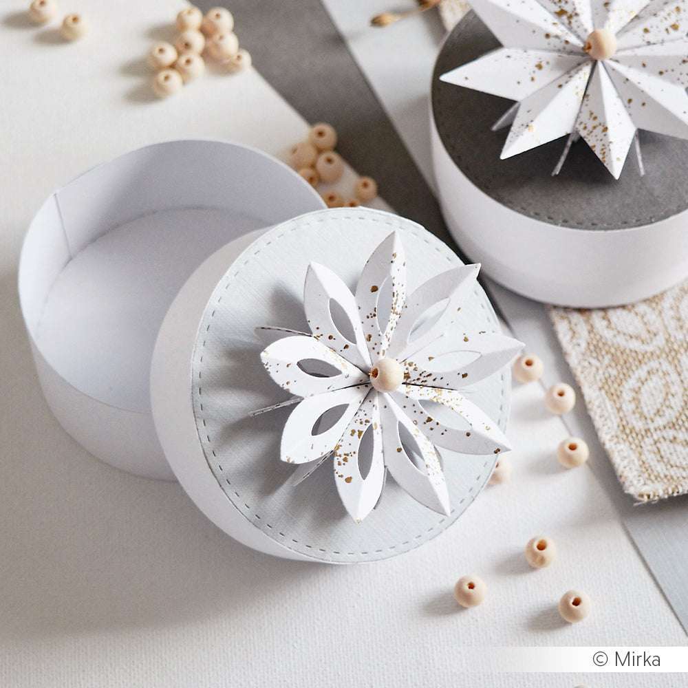 Runde weiße Geschenkschachtel mit einem 3D-Papierblumendeckel, gefertigt mit Alexandra Renke Designpapieren und Motivstanze Sternsegment Blütenform, umgeben von kleinen Holzperlen auf einer hellen Oberfläche.