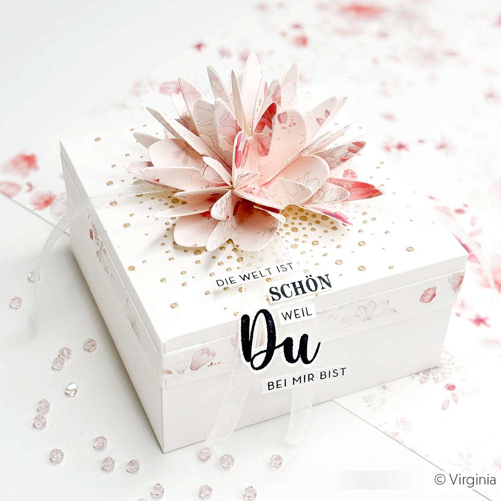 Eine weiße Geschenkbox mit einer rosa Papierblume, deutschem Text und verstreuten Perlen, elegant dekoriert mit Alexandra Renke Motivstanze Sternsegment Doppelspitze Dies.