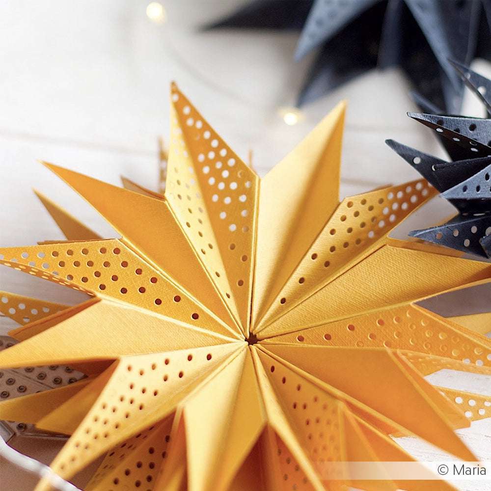 Nahaufnahme einer gelben Sterndekoration aus Alexandra Renke Designpapieren und Motivstanze Sternsegment cut-out dots, mit einem verschwommenen schwarzen Stern im Hintergrund.