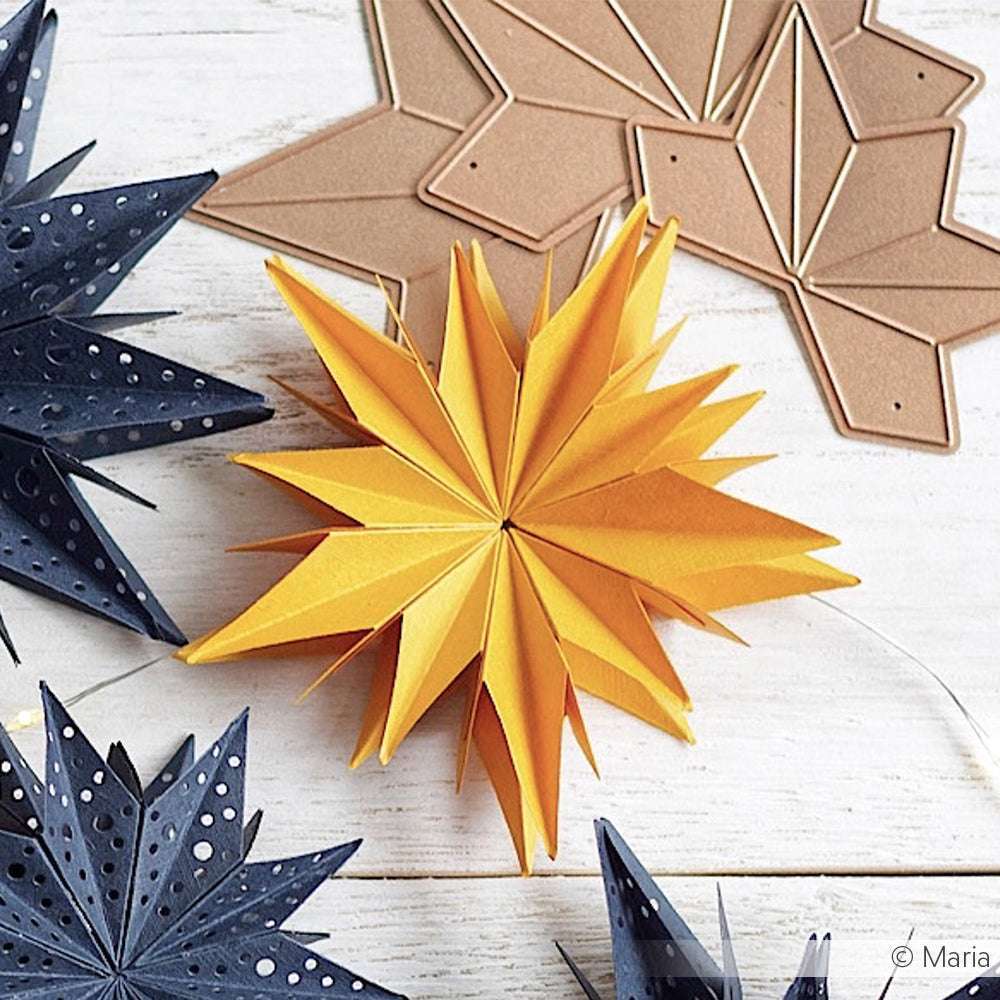 Gelbe und marineblaue Papiersterne mit perforierten Details, die mit Alexandra Renke Stanzformen wie der Motivstanze Sternsegment Stanzsysteme hergestellt wurden, liegen auf einer weißen Holzfläche mit Schablonen im Hintergrund.