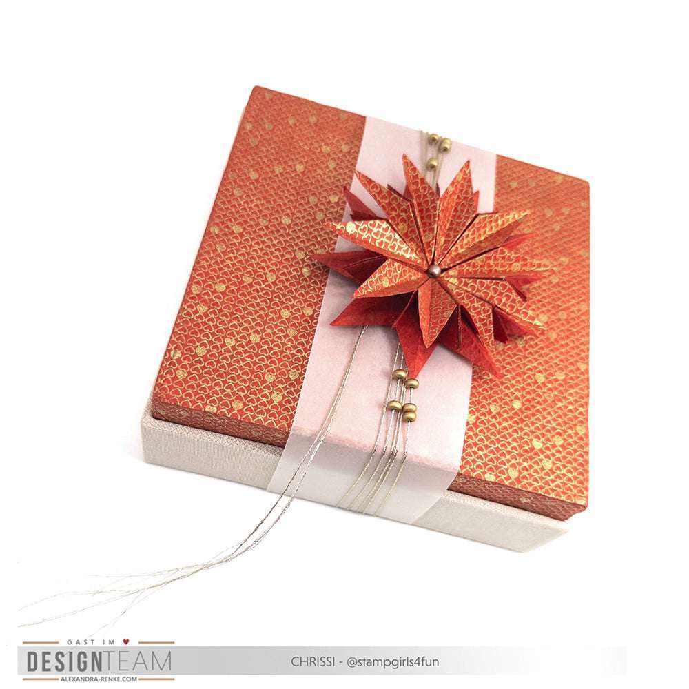 Quadratische Geschenkbox von Alexandra Renke mit orange gemustertem Deckel, weißem Band und einem detaillierten Origami-Stern aus Motivstanze Sternsegment.