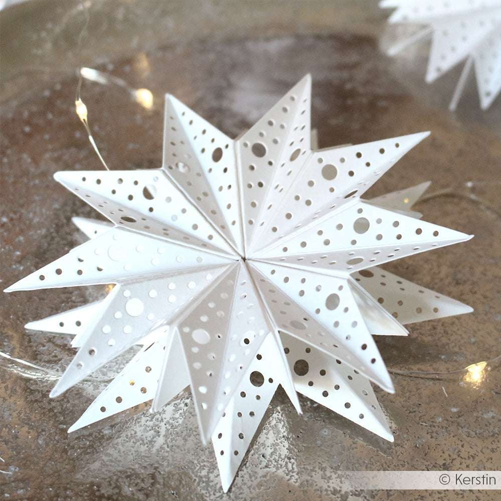Weißes Papierstern-Ornament mit perforierten Löchern, hergestellt in der Technik Motivstanze Sternsegment Punkte von Alexandra Renke, dargestellt auf einer reflektierenden Silberoberfläche.