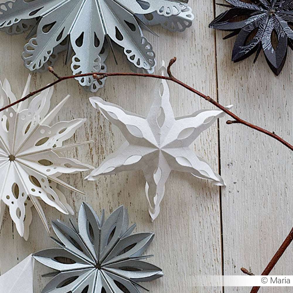 Alexandra Renke Papier-Schneeflocken-Ornamente in Weiß, Silber und Grau, hergestellt mit Motivstanze Abgerundeter Steckstern und Stanzen für Designpapier, ausgestellt auf Holz mit einem Ast.