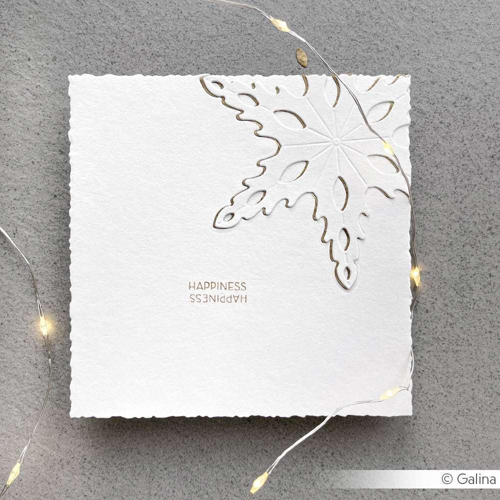 Quadratische weiße Karte von Alexandra Renke mit einer DieCut Systeme Schneeflocke und dem Wort HAPPINESS, umgeben von leuchtenden Lichterketten.