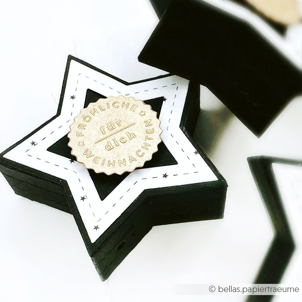 Die Alexandra Renke Black Abriss-Stern Box hat eine Sternform, ein weißes Etikett und einen Holzanhänger mit der Aufschrift Frohe Weihnachten für dich", der mit der Motivstanze Stanzsysteme gefertigt wurde.