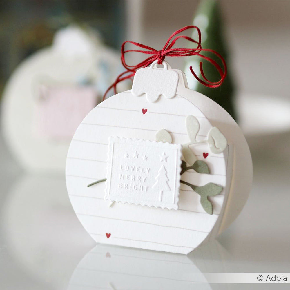 Weiße Karte in Ornamentform von Alexandra Renke mit roter Schleife, kleinen Herzen, weihnachtlichen Ausschnitten mit Stanzsystemen und Designpapieren und der Botschaft "Lovely Merry Bright".