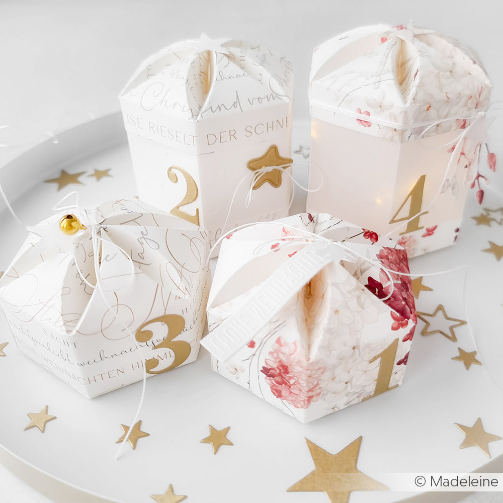 Vier dekorative, nummerierte Geschenkschachteln auf einem weißen Tablett mit goldenen Sternen, hergestellt mit Alexandra Renke Designpapieren und einer Schachtelausstanzung mit Blumenverschluss - ideal für einen Adventskalender.