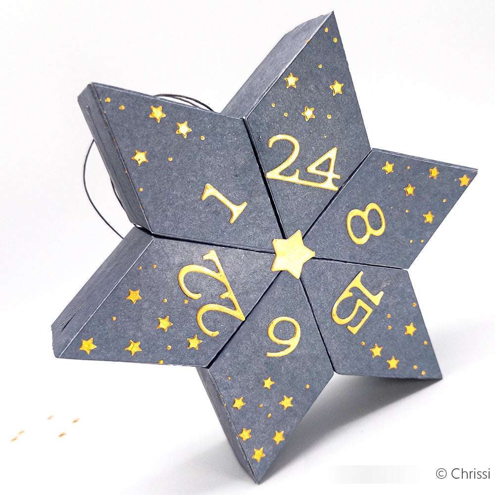 Eine mit DieCut Systemen hergestellte Alexandra Renke-Sternschachtel mit nummerierten Klappen und goldenen Sternen - wie ein Adventskalender.