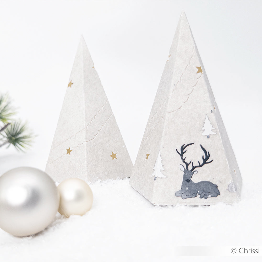 Zwei Weihnachtsbaumkugeln aus Papier von Alexandra Renke, die mit Designpapieren und Stanzsystemen hergestellt wurden, liegen zwischen Tannennadeln und Silberkugeln im Schnee.