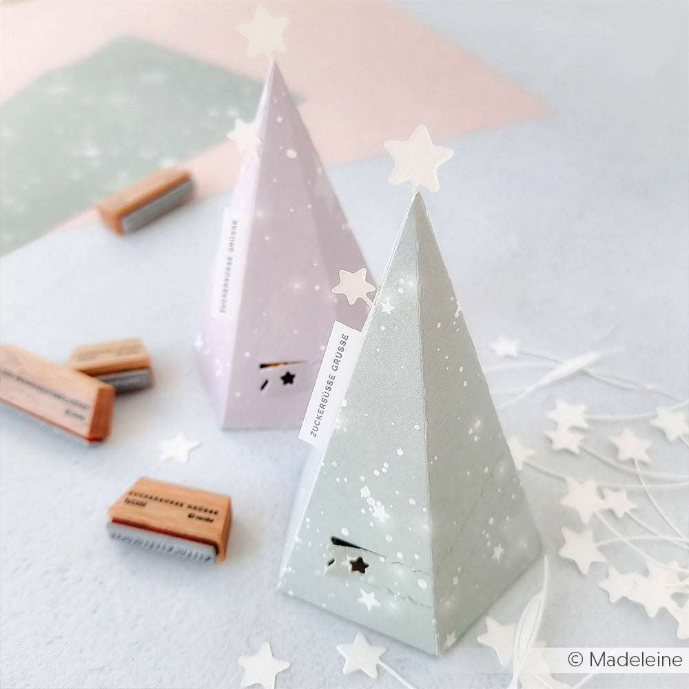 Zwei pastellfarbene Pyramiden-Geschenkboxen aus Alexandra Renke Designpapieren, umgeben von Sternausschnitten und Stempeln, hergestellt mit der Motivstanze Tannen Abriss-Box DieCut Systeme.