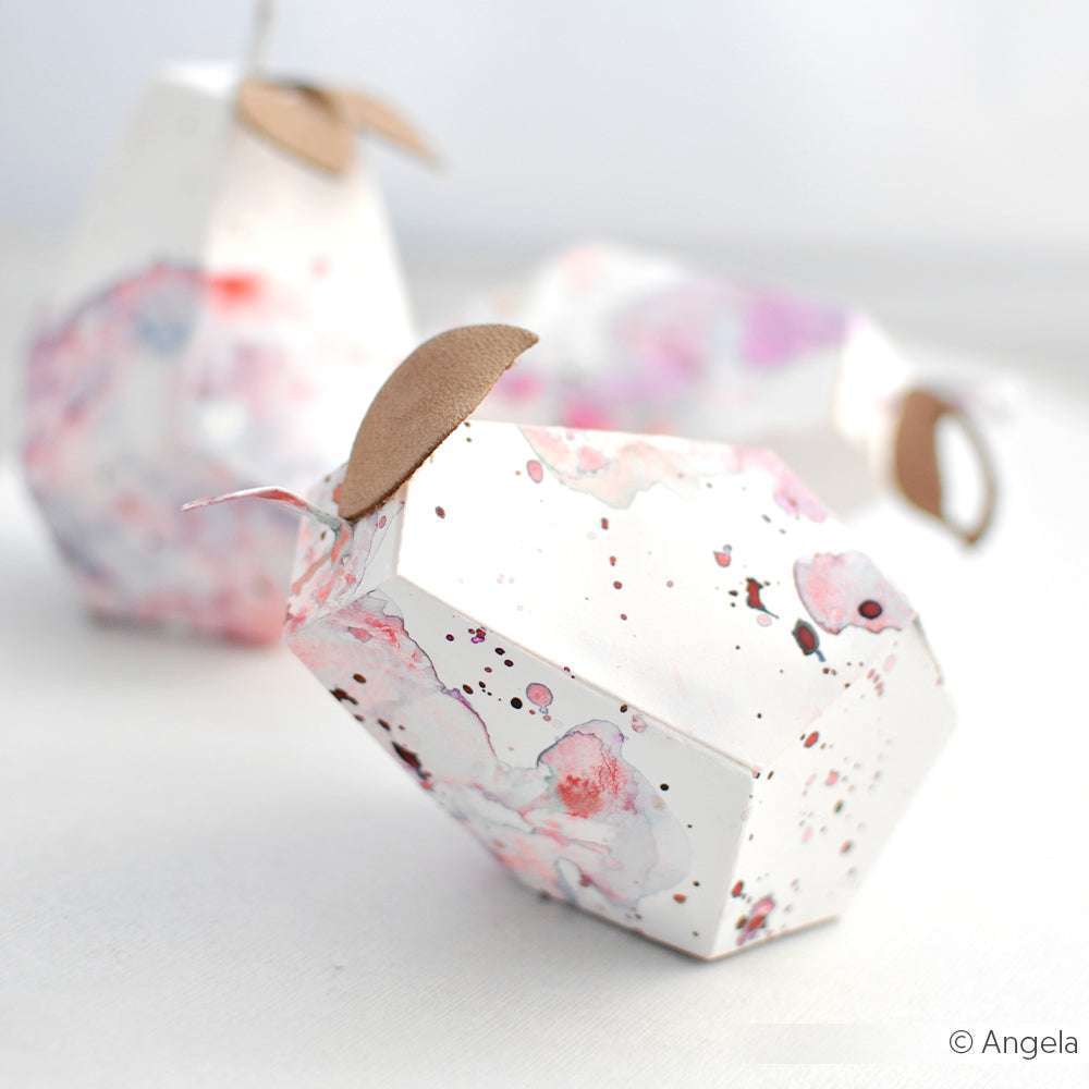 Geometrische Birnenboxen von Alexandra Renke Designpapiere mit Aquarelltupfen und braunen Papierblättern werden mit der Motivstanze Birnen Box DieCut Systeme kunstvoll auf einer weißen Fläche arrangiert.