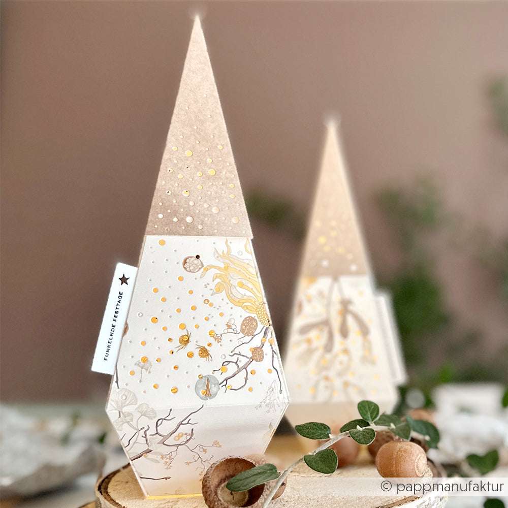 Zwei baumförmige Papierlaternen von Alexandra Renke, die mit PAPPcut®ies und Deep Edge Motivstanzen hergestellt wurden, zeigen goldene Akzente und Naturmotive auf einem mit Eicheln und Blättern geschmückten Tisch.