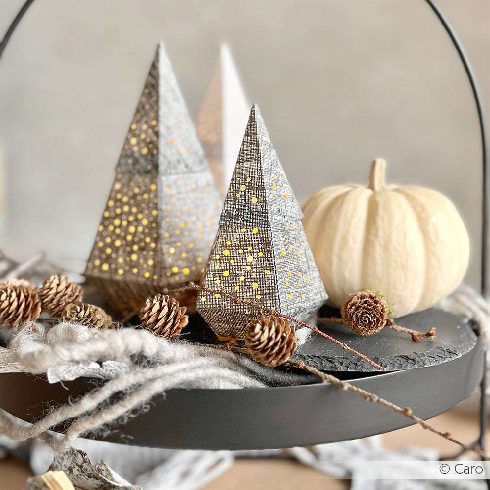 Papierbäume mit winzigen Lichtern, ein weißer Kürbis und Tannenzapfen auf einem runden Tablett schaffen eine gemütliche, festliche Szene - wunderschön akzentuiert mit Alexandra Renkes PAPPcut®ies und Deep Edge Motivstanzen für zusätzlichen Charme.