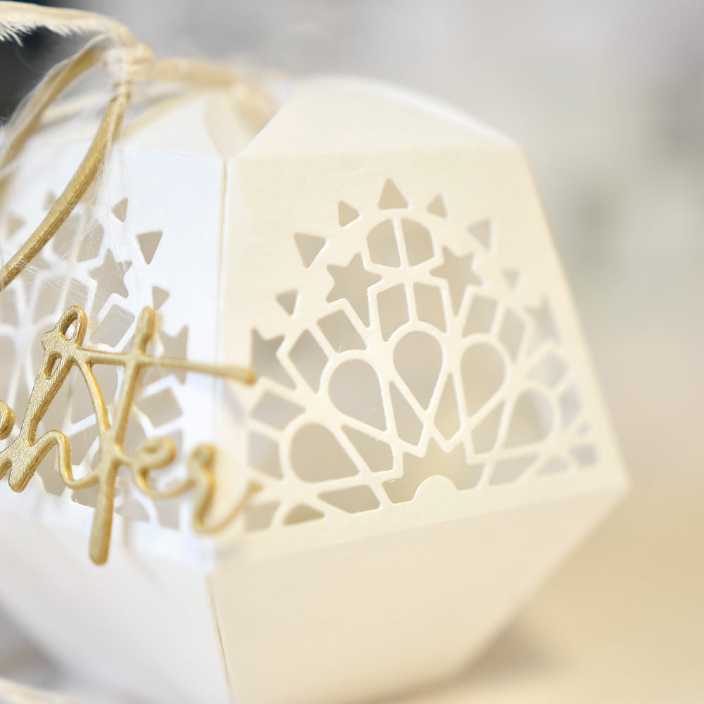 Weiße, geometrische Papierlaterne von Alexandra Renke mit verschlungenen Stern- und Herzausschnitten aus Deep Edge Motivstanzen und PAPPcut®ies, gebunden mit Schnur und einem goldenen Schriftzug für einen charmanten dekorativen Akzent.