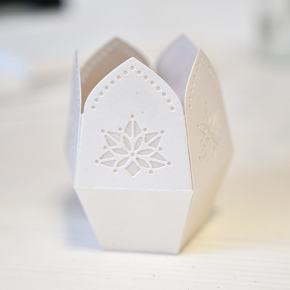 Weiße Papierlaterne oder Geschenkbox von Alexandra Renke mit kunstvollen Schneeflockenmotiven, die mit Deep Edge Motivstanzen und der PAPPcut®ies-Technik hergestellt wurden und auf einer hellen Oberfläche präsentiert werden.