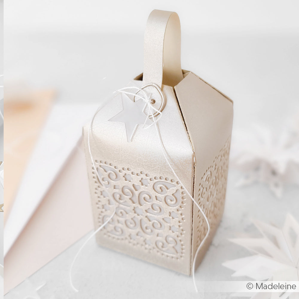 Elegante goldene Geschenkschachtel mit dekorativem Muster, gekrönt von einem Sternanhänger und weißer Kordel von Alexandra Renke, inspiriert von PAPPcut®ies und Deep Edge Motivstanzen für ein raffiniertes Finish auf hellem Hintergrund.